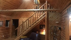 A wooden cabin interior with a staircase, a leather chair, and a ski rack.