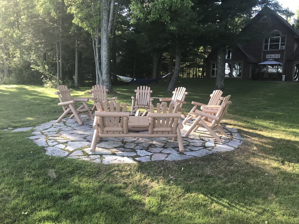A wooden Adirondack chair set on a stone patio surrounded by grass, with a hammock and a building in the background.