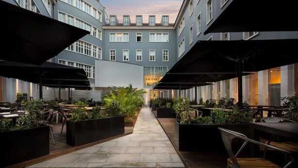 An outdoor dining area with tables and chairs, surrounded by planters and umbrellas, leading to a building with large windows. - Dom Luis I Prestige Flat 18 (Lisboa)