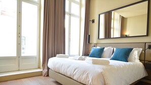 A hotel room with a large bed, a window with curtains, a wall-mounted mirror, and a bedside table with a lamp. - Dom Luis I Prestige Flat 18 (Lisboa)