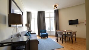 A modern living room with a sofa, a dining table with chairs, a TV mounted on the wall, and a large window with curtains. - Dom Luis I Prestige Flat 18 (Lisboa)