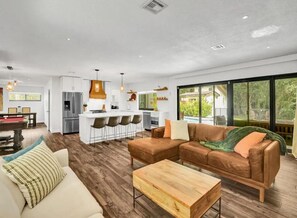A modern living room with a brown leather sofa, wooden coffee table, and a dining area with bar stools.