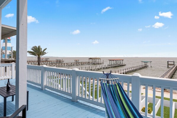 Ein Balkon mit Blick auf den Strand, einer Hängematte und einem Tisch mit einer Flasche.