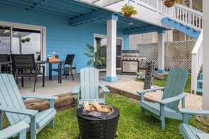 Eine überdachte Terrasse im Freien mit Adirondack-Stühlen, einem Grill und einer Feuerstelle.