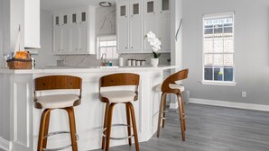 Una cocina moderna con armarios blancos, salpicadero de mármol y una isla central con taburetes de bar.