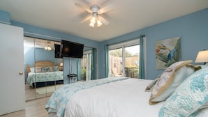 A bedroom with a large bed, a ceiling fan, a TV, and a sliding glass door leading to an outdoor area. - New Smyrna Beach Townhouse/flagler Ave/beach/walk Everywhere and Pet Friendly! (New Smyrna Beach)