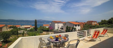 A terrace with a table set for breakfast, overlooking a coastal village with houses and a clear sky.