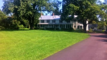 Traditional two-story house with a spacious porch, set amidst a serene and lawn with mature trees.