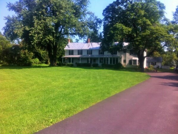 Traditional two-story house with a spacious porch, set amidst a serene and lawn with mature trees.