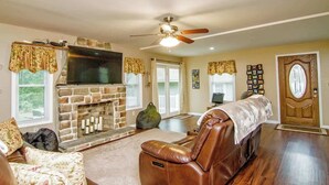 A living room with a stone fireplace, leather sofa, and a television. - Cabin by the Creek with private creek access - (Tannersville)
