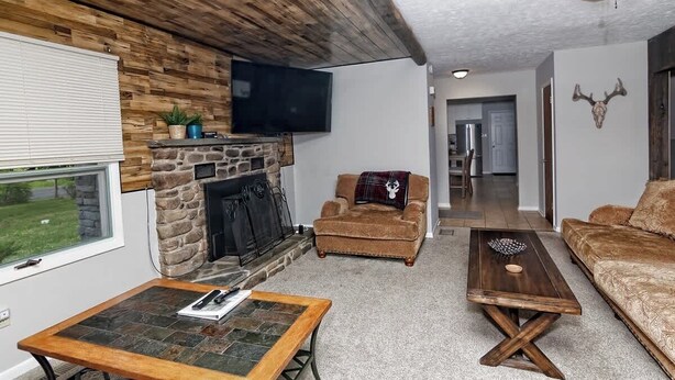 Un salon chaleureux avec une cheminée en pierre, un téléviseur fixé au mur et un ventilateur de plafond.
