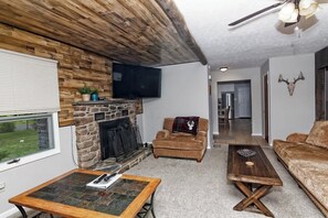 A cozy living room with a stone fireplace, a television mounted on the wall, and a ceiling fan.