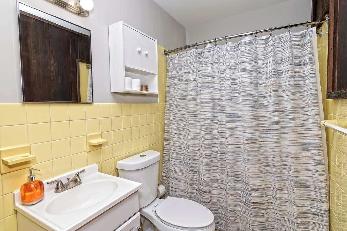 Une salle de bain équipée de toilettes, d’un lavabo, d’un miroir et d’un rideau de douche à rayures.