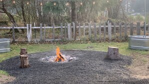 A fire pit surrounded by gravel, a wooden fence, and string lights in a wooded area. - Packwood’s BaseCamp@MtRainier 2bd/2bth-pets (Packwood)