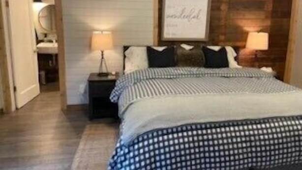 A bedroom with a bed, two bedside tables, a nightstand, a wall-mounted artwork, and a wooden door. - Packwood’s BaseCamp@MtRainier 2bd/2bth-pets (Packwood)