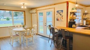 A spacious kitchen with a dining area, featuring a wooden table and chairs, a built-in island with a sink, and a view of the outdoors through large windows. - Packwood’s BaseCamp@MtRainier 2bd/2bth-pets (Packwood)