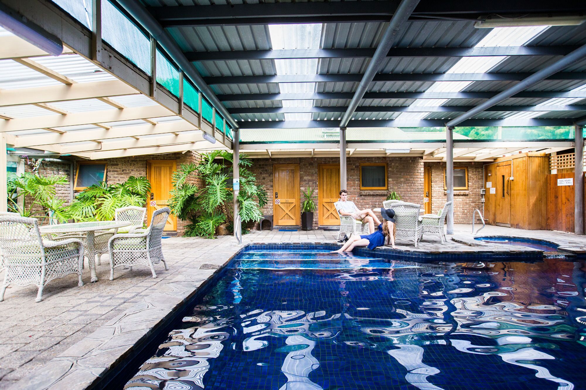 An indoor swimming pool with a tiled floor, surrounded by wicker furniture and potted plants.