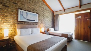 A hotel room with a brick wall, a large bed, a smaller bed, a wooden door, and a framed artwork above the larger bed. - The Lodge by Haus (Adelaide)