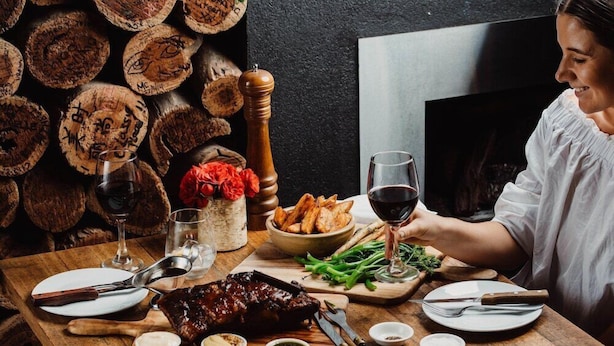 A dining table set with a steak, potatoes, green beans, and wine glasses. - The Lodge by Haus (Adelaide)
