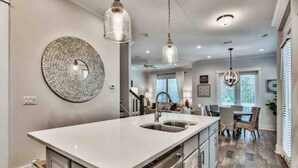 A modern kitchen with a central island, pendant lighting, and a dining area with wicker chairs.