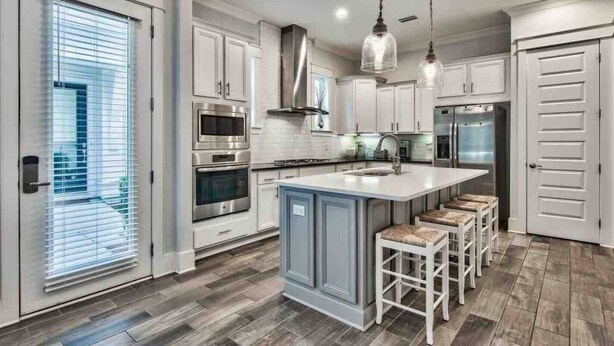 A modern kitchen with white cabinetry, stainless steel appliances, and a central island with bar stools.