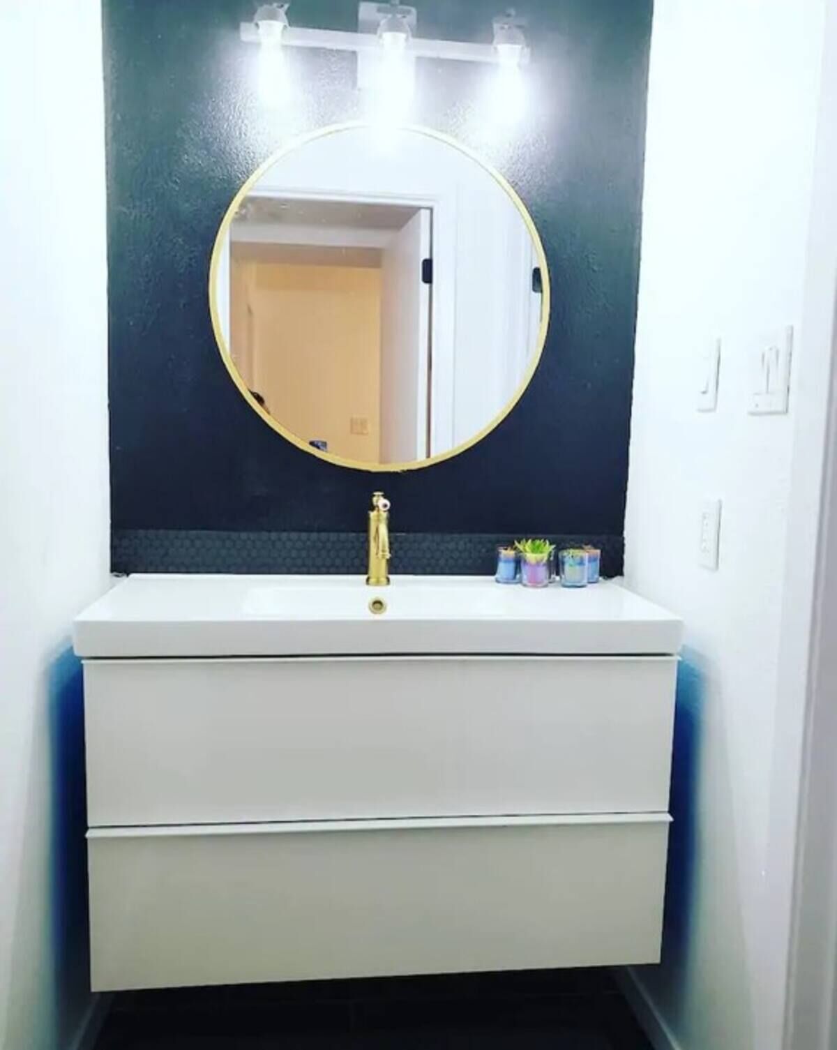 A bathroom vanity with a round mirror, a gold faucet, and a white countertop.