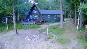 A cabin with a deck, surrounded by trees. - A-Frame cabin located on the shores on lake Independence. (Big bay)