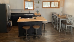 A modern kitchen with a central island, bar stools, and a dining area with a table and chairs. - A-Frame cabin located on the shores on lake Independence. (Big bay)