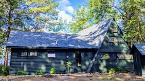 A cabin with a steeply pitched roof, surrounded by trees. - A-Frame cabin located on the shores on lake Independence. (Big bay)