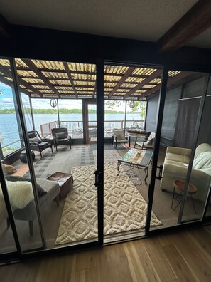 A room with a glass partition, a view of a lake, a wooden deck, and a seating area with chairs and a table.