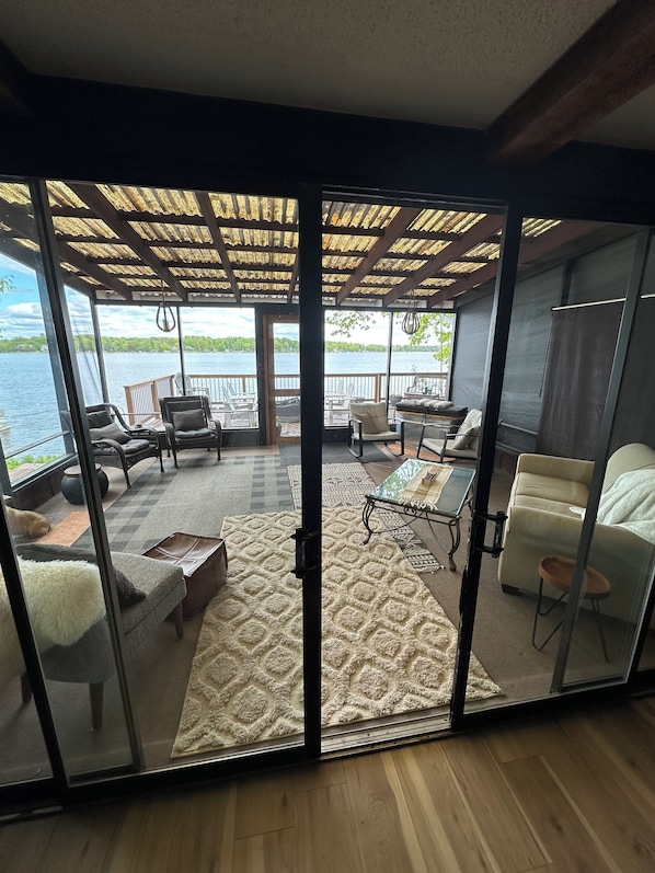 A room with a glass partition, a view of a lake, a wooden deck, and a seating area with chairs and a table.