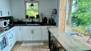 A modern kitchen with white cabinets, a wooden dining table, and a view of the outdoors. - Top-Rated Balsam Lake Vacation Home with Stunning Lake Views, 4 BR & Family Fun (Balsam Lake)