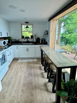 A modern kitchen with white cabinets, a wooden dining table, and a view of the outdoors.