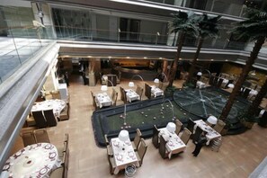 Espaço amplo e interno com vários níveis, mesas e cadeiras para refeições, mesa de bilhar e palmeiras.
