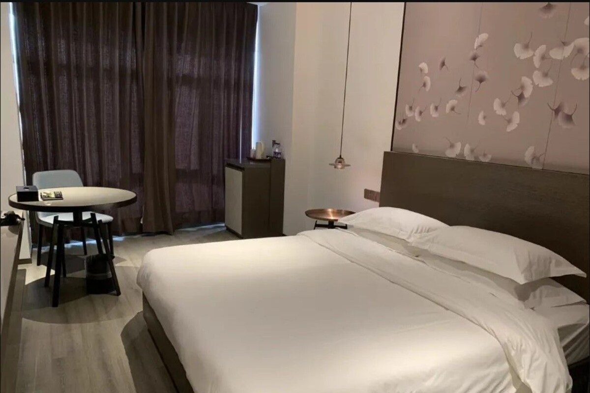 Habitación de hotel con una cama grande, un escritorio con silla, una mesita pequeña y un panel decorativo en la pared.