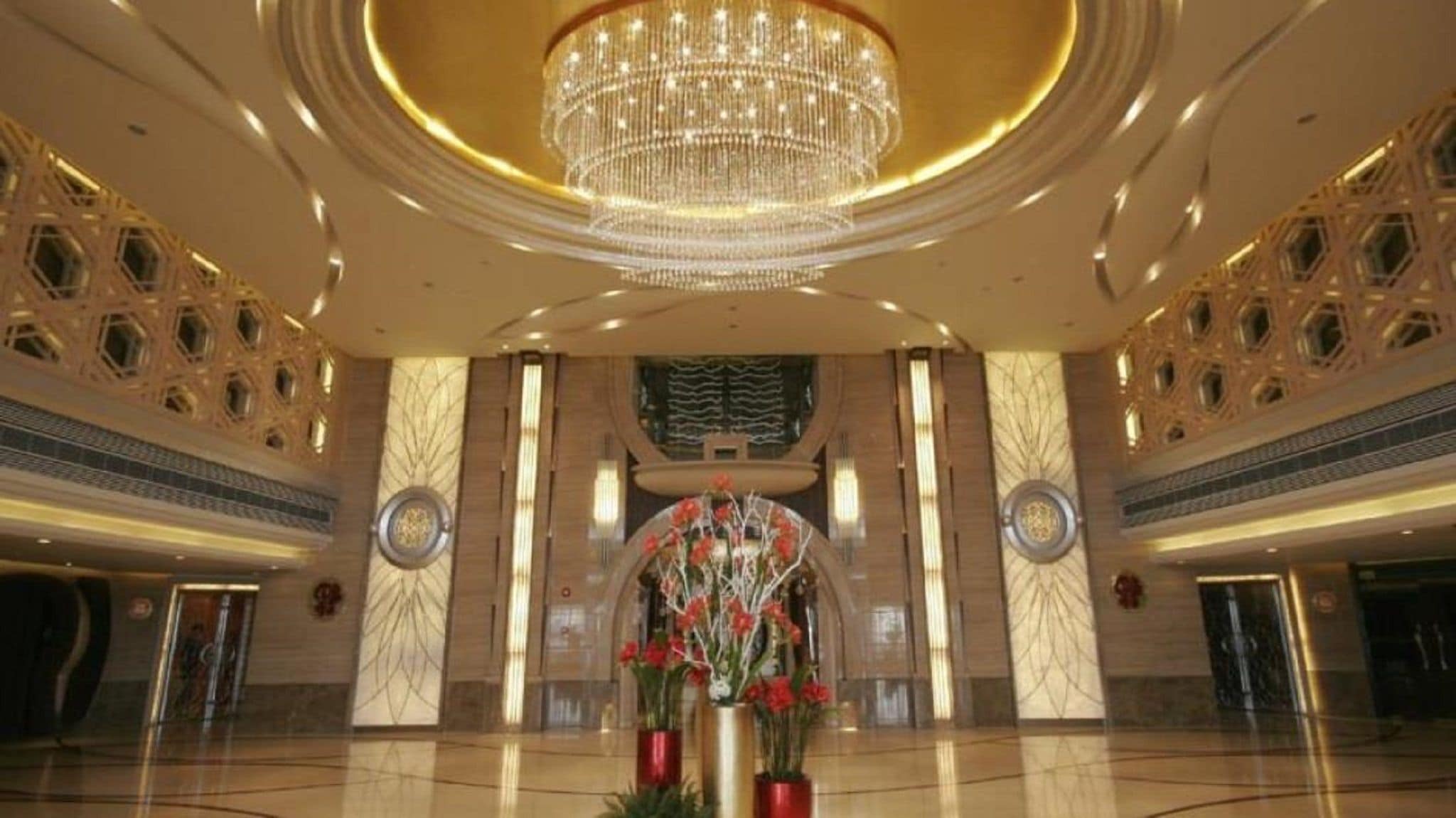 A spacious lobby with a large chandelier, marble walls, and a floral arrangement.