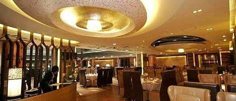A spacious restaurant with a central circular ceiling design, multiple dining tables, and a warm ambiance.