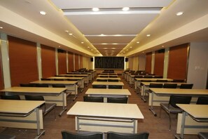 A conference room with rows of tables and chairs, a stage at the front, and a high ceiling with recessed lighting. - Da Zhong Airport Hotel (Shanghai)