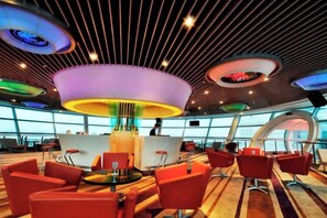 Uma área de estar moderna com um bar central, assentos vermelhos e um design de teto único.