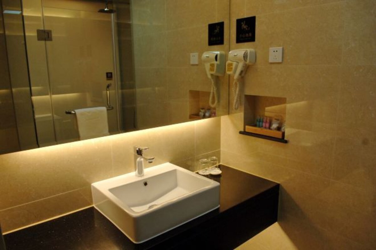 Un baño moderno con un espejo grande, un lavamanos blanco y dos secadores de pelo montados en la pared.