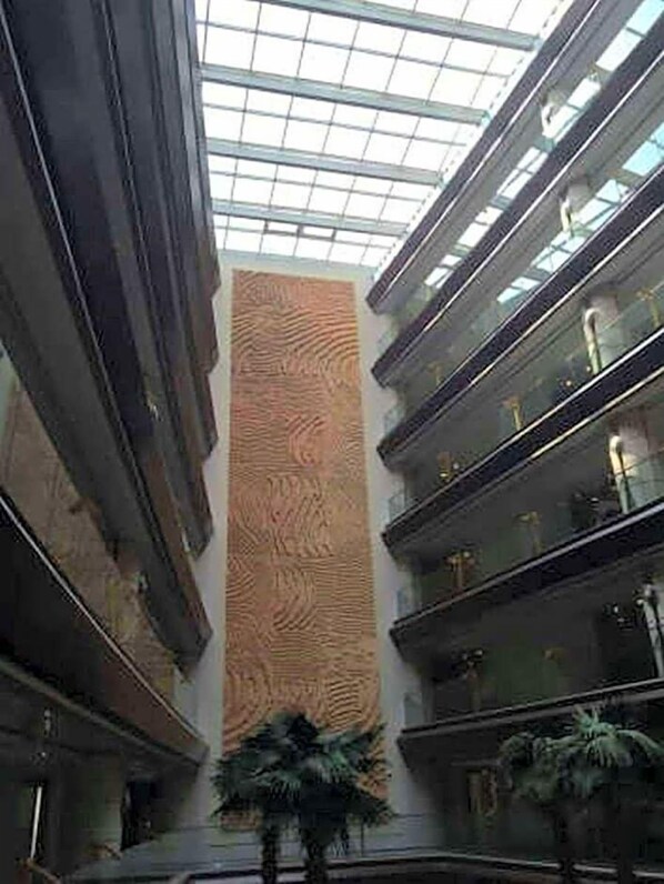 Un interior moderno con un elemento vertical central, barandillas de vidrio y plantas en macetas.