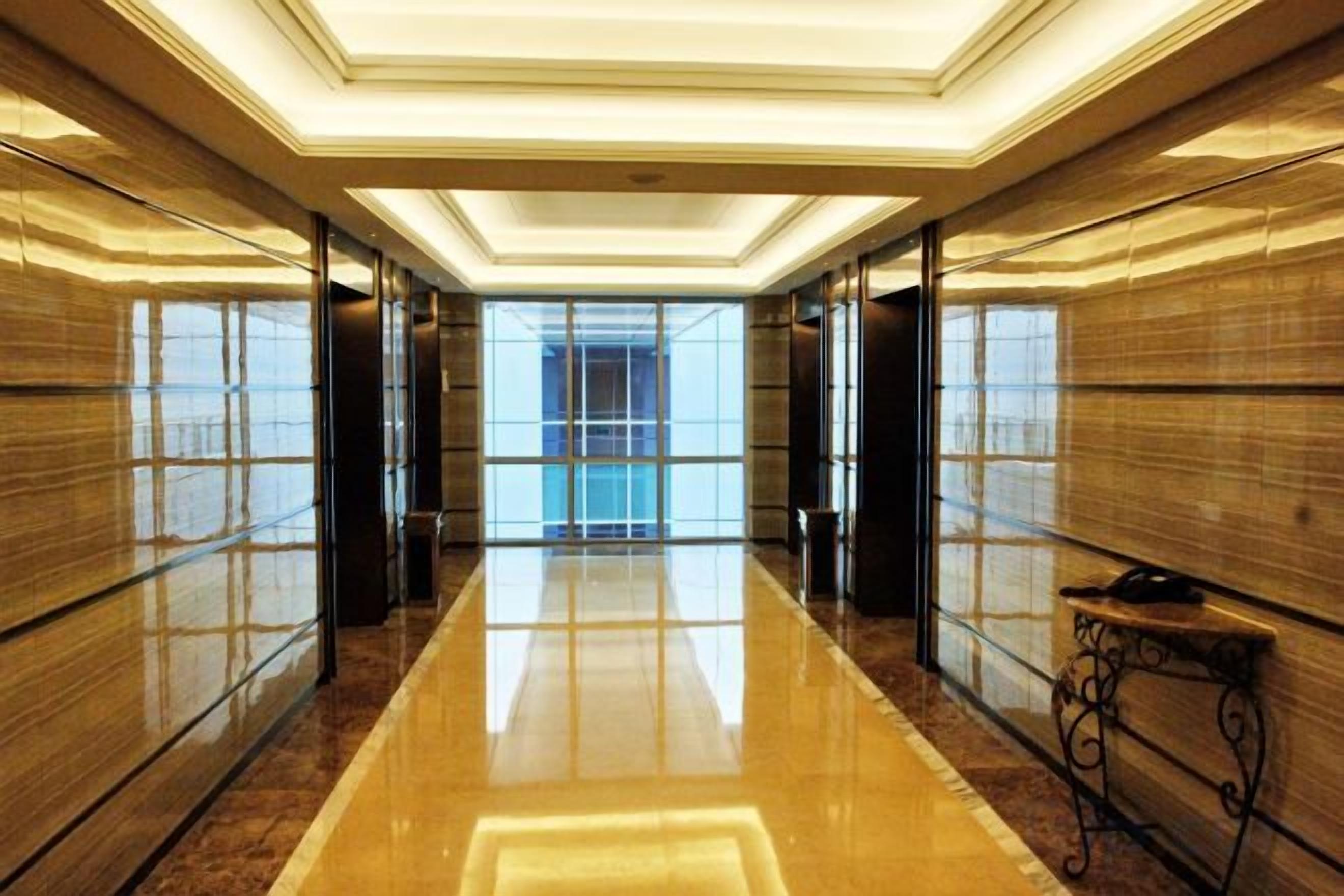 A long, polished corridor with reflective flooring, flanked by wooden panel walls and a bench with a telephone.