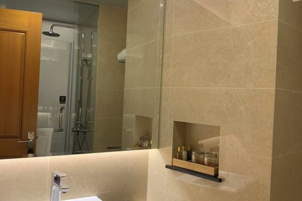 Un baño moderno con ducha envuelta en vidrio, tocador con espejo y repisa con artículos de aseo.