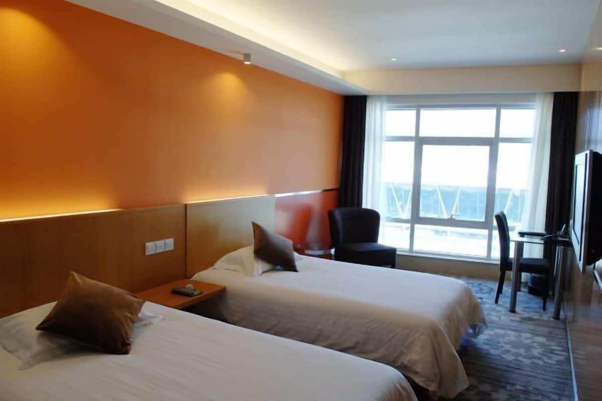 A hotel room with two beds, a desk, a chair, and a large window.