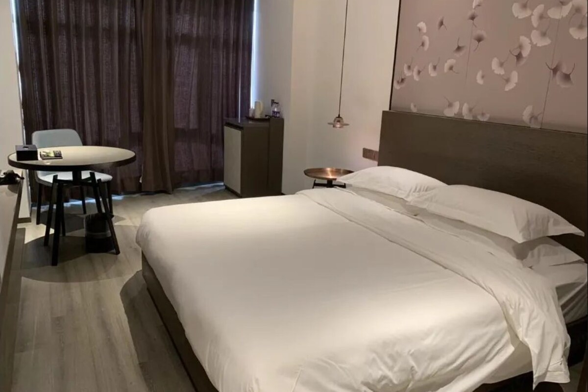 A hotel room with a large bed, a desk with a chair, a small table, and a decorative wall panel.