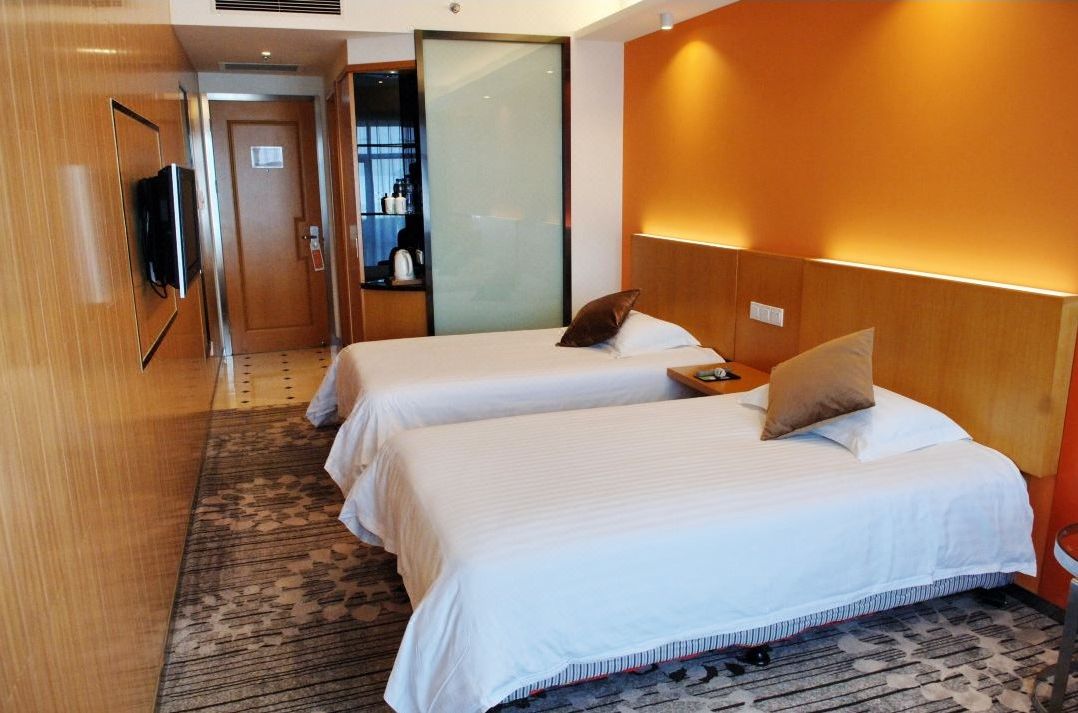 Ein Hotelzimmer mit zwei Betten, einem Fernseher, einer Minibar und einem Badezimmer mit Glastür.