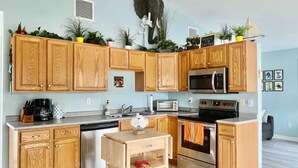 A kitchen with wooden cabinets, a microwave, a toaster, and a stove. There are plants on the cabinets and a small table with a vase.