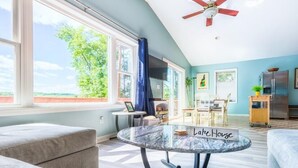 A spacious living room with a large window, a ceiling fan, and a table labeled "Lake House".