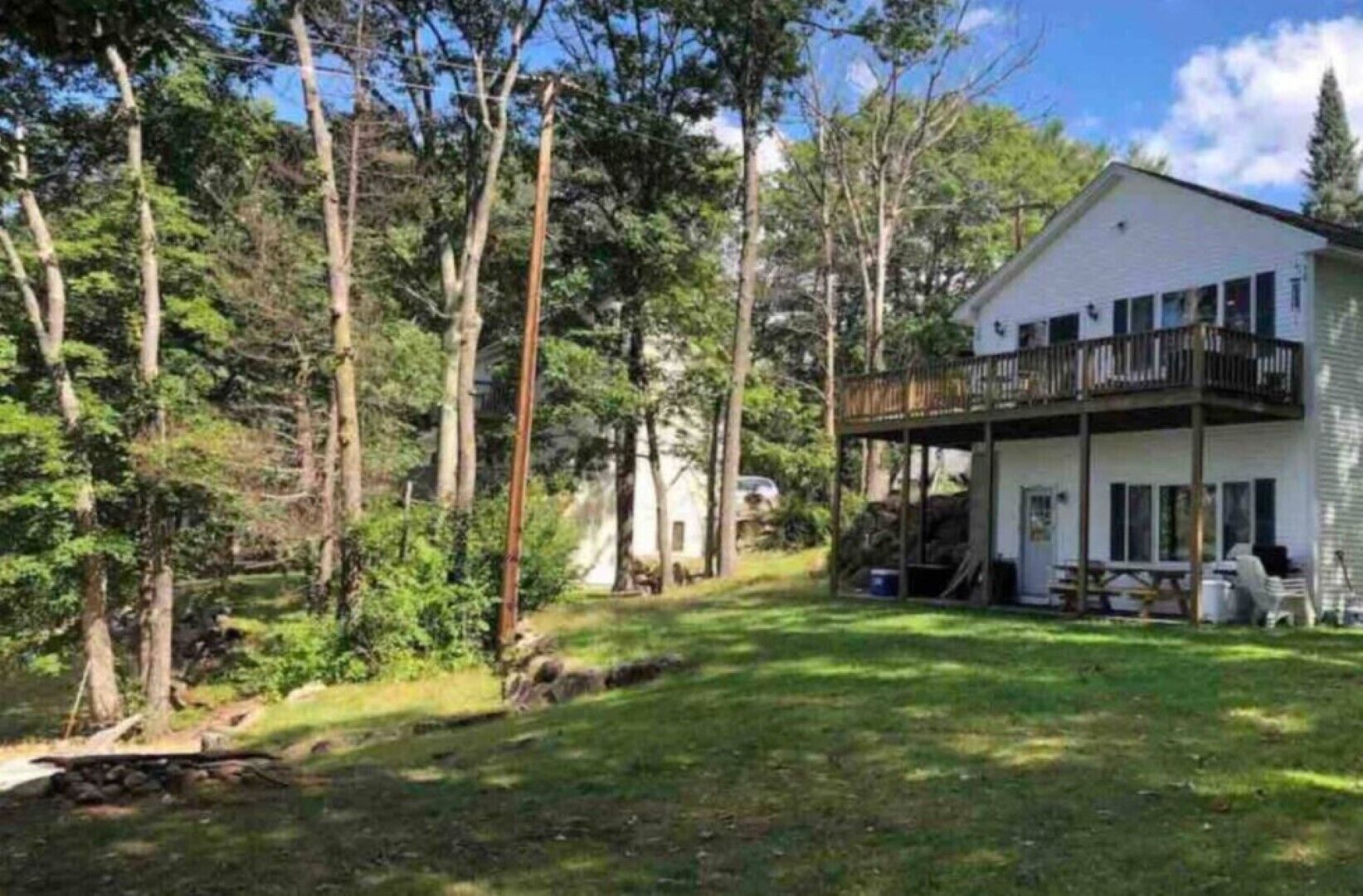 Une maison dotée d’un porche abrité et d’une cour verdoyante, entourée de grands arbres.