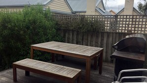 Eine Holzterrasse mit Tisch und Bank, einem Grill und einem Holzzaun.